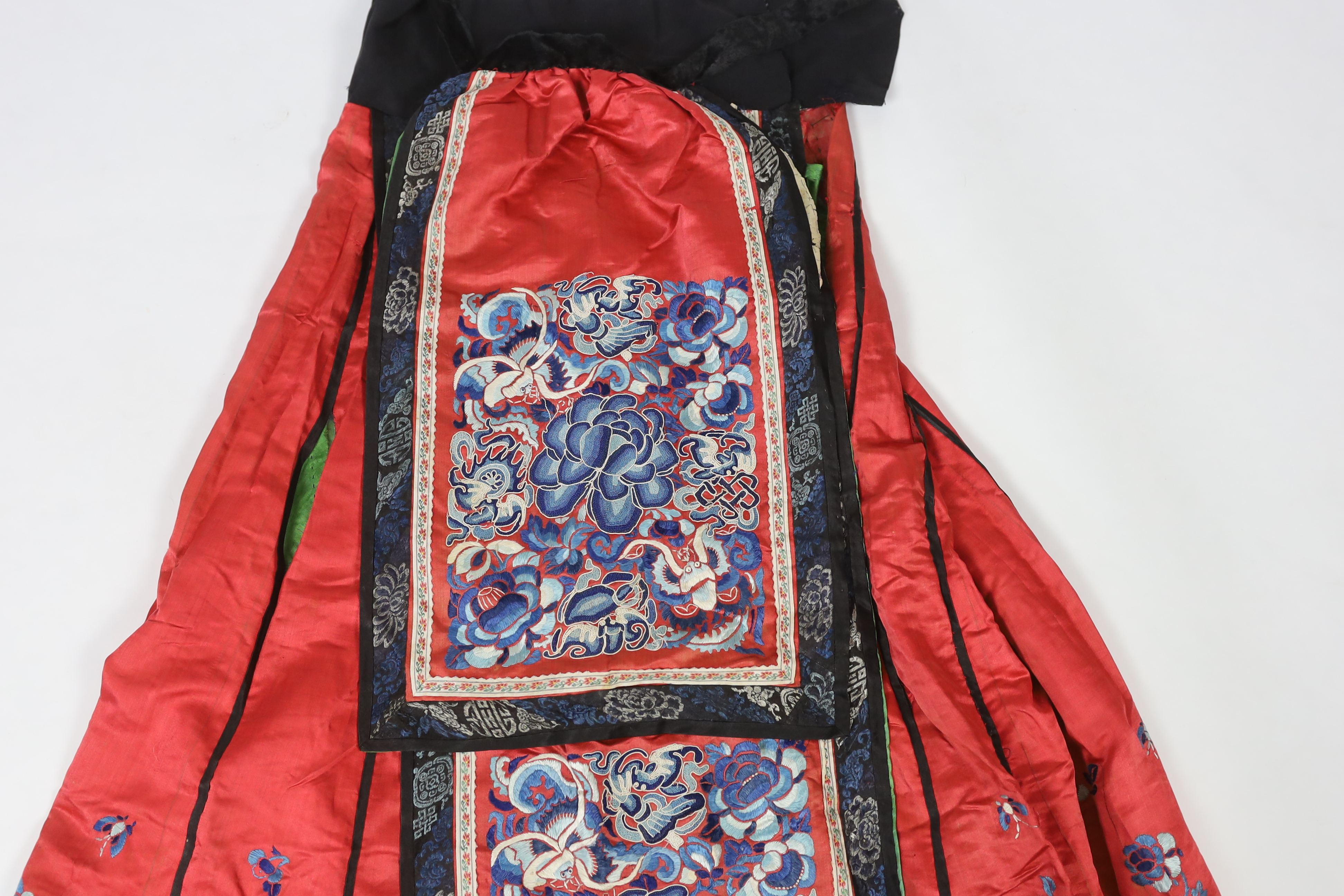 A Chinese red silk skirt, embroidered with a blue silk panel of Chinese knotting flowers and auspicious symbols, the bottom of the skirt with spot motifs bordered with embroidered braiding and ribbon, the slant is lined